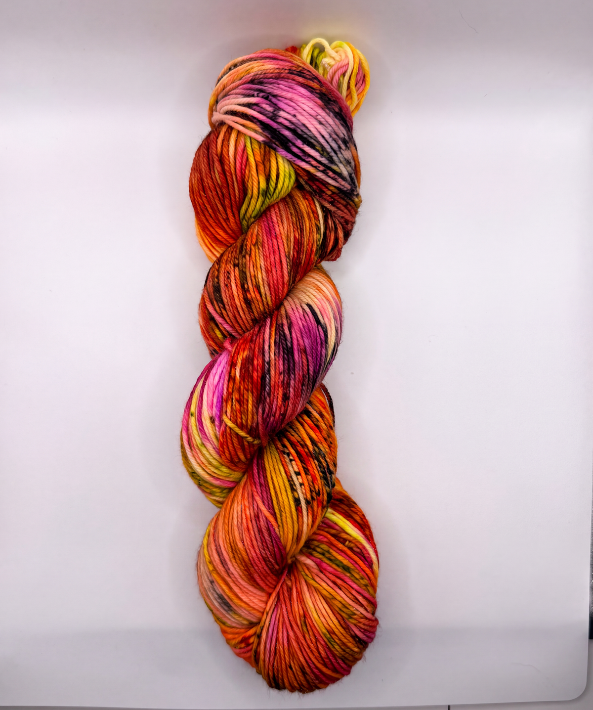 A single hank of variegated yarn with a bright multicolor pattern of pink, orange, yellow, red, and purple, photographed vertically against a plain white background.