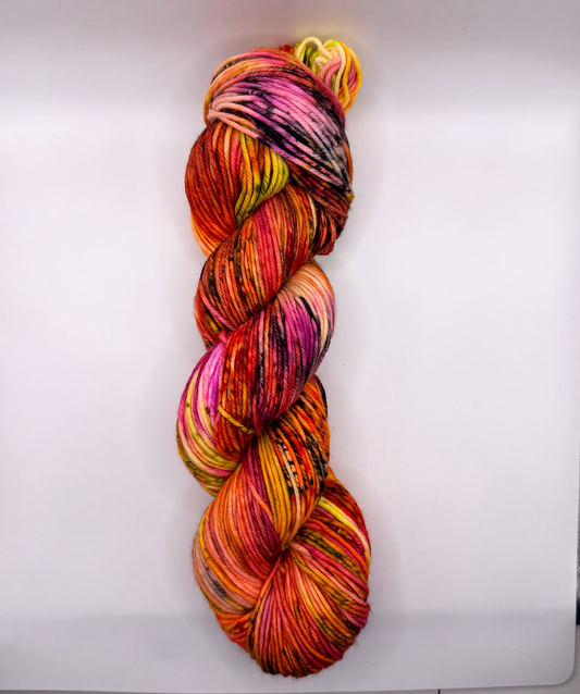 A single hank of variegated yarn with a bright multicolor pattern of pink, orange, yellow, red, and purple, photographed vertically against a plain white background.