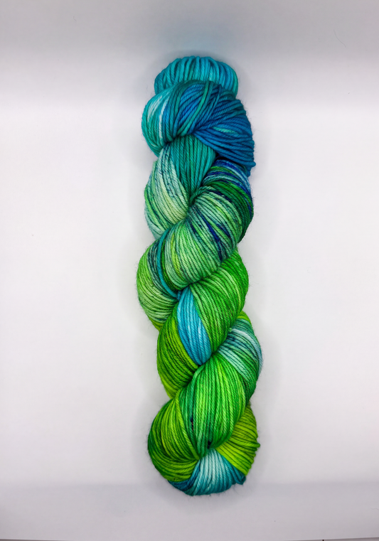 A single hank of variegated yarn in shades of green, blue, and teal, photographed vertically against a plain white background.