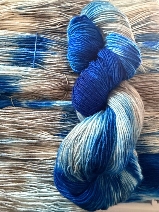 A close-up of a skein of variegated yarn in shades of blue, silver and white, placed on top of a larger bundle of similar yarn.