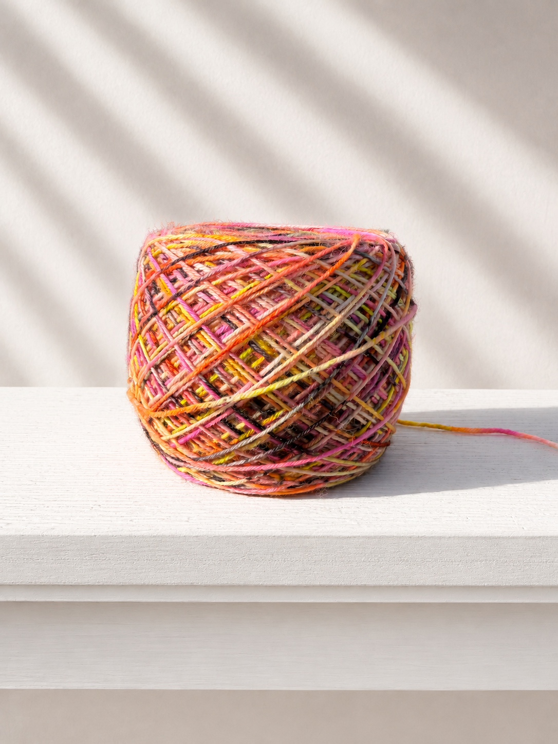 A variegated hand-dyed yarn cake speckled with yellow, orange, pink and black colors set on a sunny ledge.
